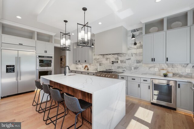 kitchen featuring light stone counters, an island with sink, a notable chandelier, light hardwood / wood-style flooring, and stainless steel appliances