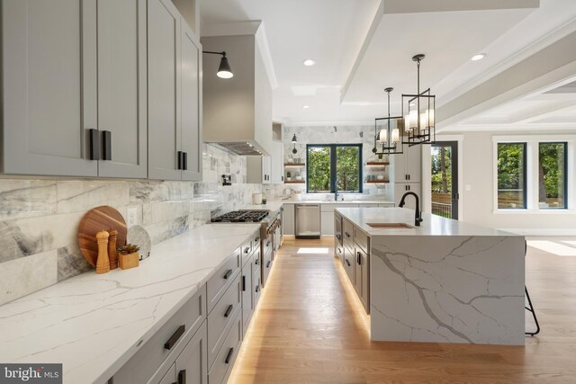 kitchen featuring light stone countertops, ornamental molding, a large island with sink, and stainless steel dishwasher