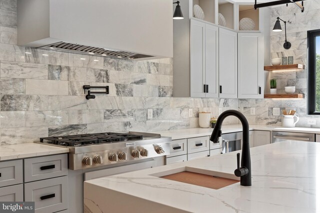 kitchen with light stone counters, pendant lighting, custom exhaust hood, sink, and appliances with stainless steel finishes