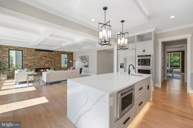 kitchen with appliances with stainless steel finishes, hanging light fixtures, white cabinetry, a fireplace, and a center island with sink