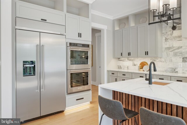 kitchen with white cabinetry, hanging light fixtures, light hardwood / wood-style flooring, stainless steel appliances, and light stone countertops