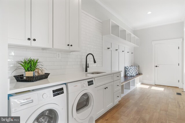 washroom with light wood-type flooring, crown molding, cabinets, sink, and washing machine and clothes dryer