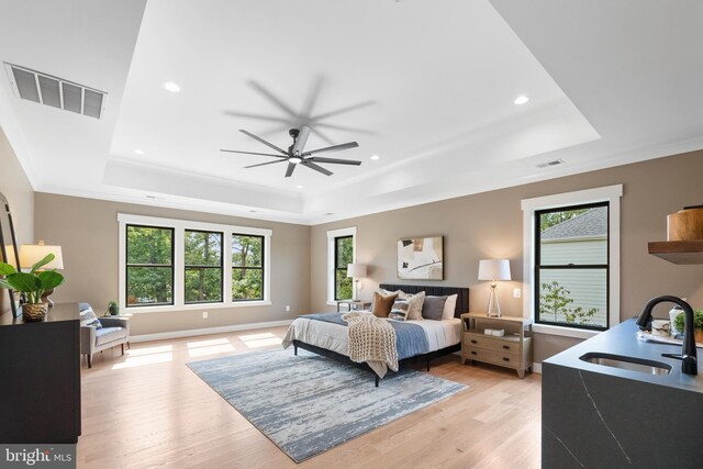 bedroom with light wood-type flooring, a tray ceiling, multiple windows, and sink