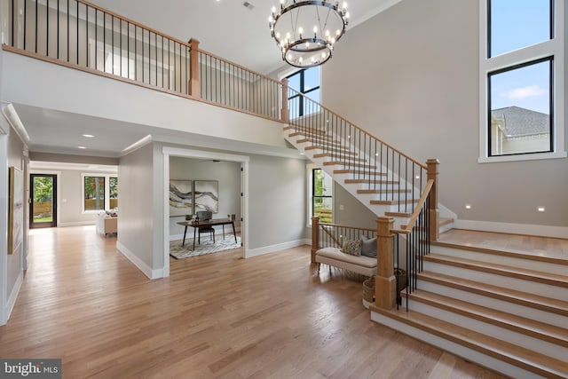 staircase featuring wood finished floors, a towering ceiling, baseboards, an inviting chandelier, and crown molding