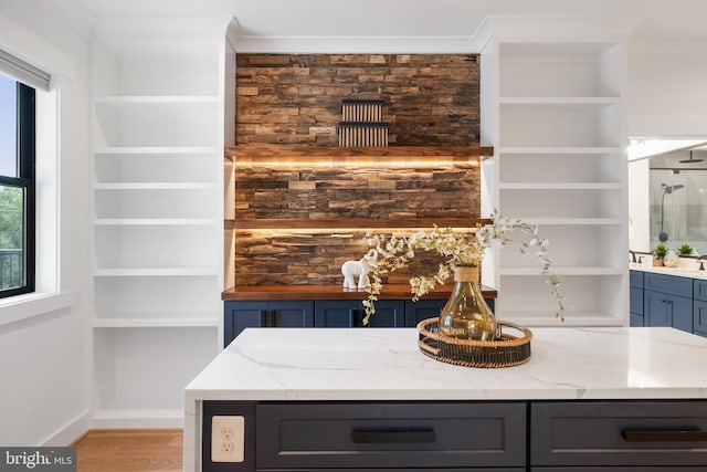 bar with light stone counters, light hardwood / wood-style flooring, and crown molding