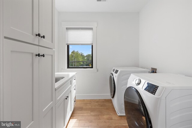 washroom with washer and clothes dryer, cabinets, and light wood-type flooring