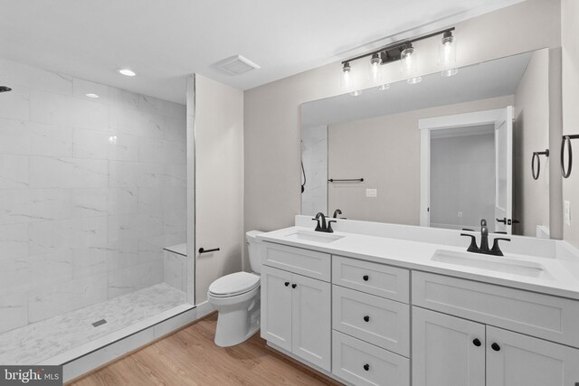 bathroom featuring a tile shower, hardwood / wood-style flooring, vanity, and toilet