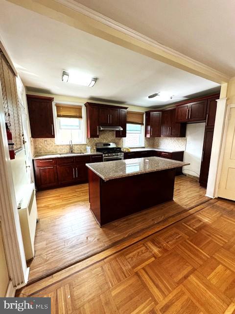 kitchen with dark stone countertops, stainless steel stove, sink, a kitchen island, and tasteful backsplash