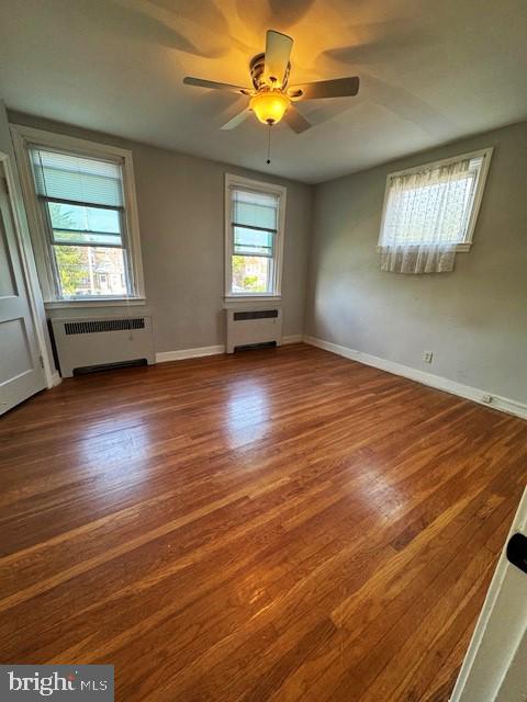 empty room featuring ceiling fan, hardwood / wood-style floors, and radiator heating unit