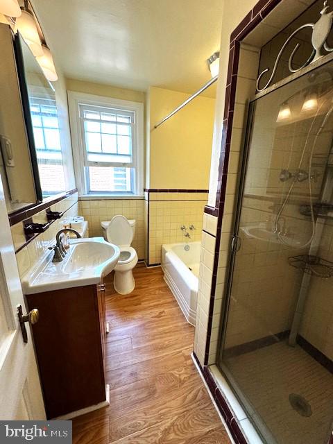 full bathroom with tile walls, independent shower and bath, toilet, and vanity