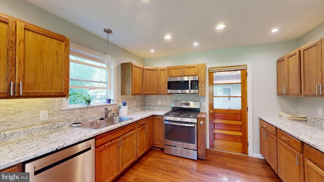 kitchen featuring pendant lighting, a sink, light wood-style floors, appliances with stainless steel finishes, and decorative backsplash