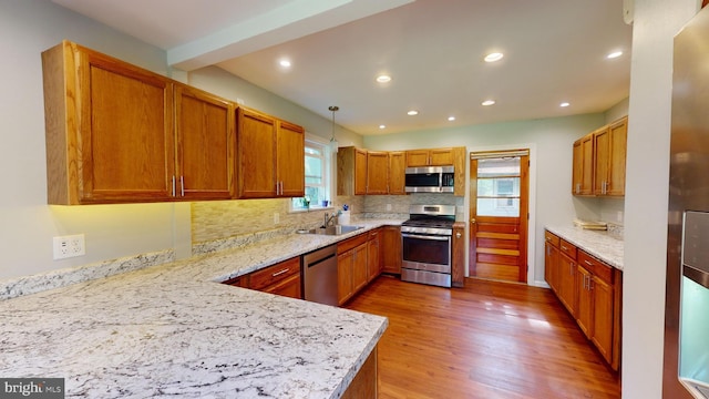 kitchen featuring a sink, tasteful backsplash, wood finished floors, appliances with stainless steel finishes, and light stone countertops