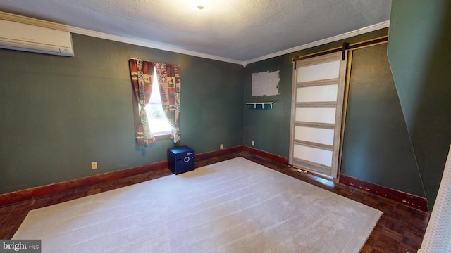 empty room featuring a wall mounted AC, a textured ceiling, a barn door, crown molding, and baseboards