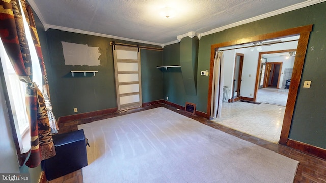 empty room with a barn door, baseboards, a textured ceiling, and ornamental molding