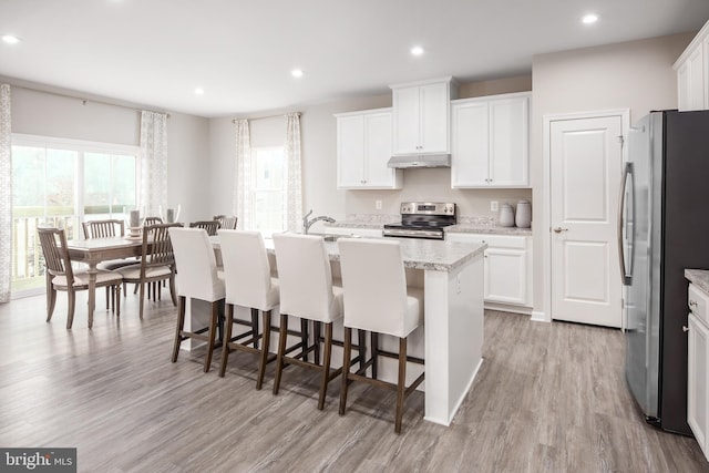 kitchen with light wood-type flooring, white cabinets, appliances with stainless steel finishes, a kitchen bar, and a center island with sink