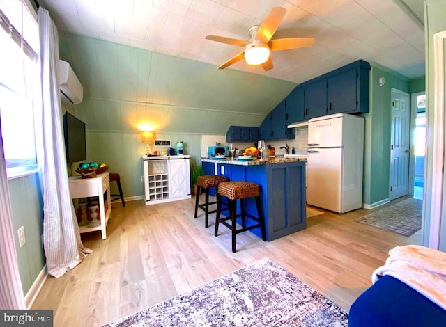 kitchen featuring white refrigerator, light hardwood / wood-style flooring, blue cabinetry, a wall mounted AC, and a breakfast bar area