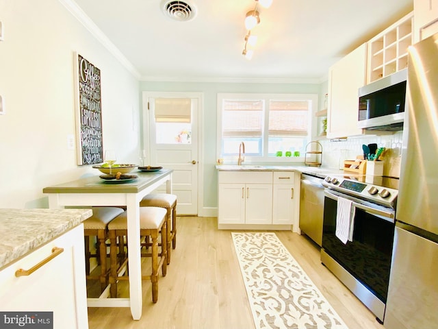 kitchen with appliances with stainless steel finishes, light wood-type flooring, backsplash, crown molding, and white cabinets