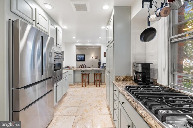 kitchen with white cabinets, light stone counters, stainless steel appliances, and tasteful backsplash