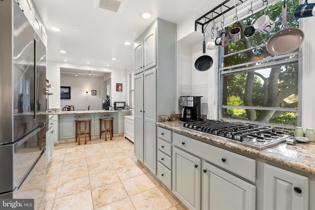 kitchen with gray cabinets, tasteful backsplash, light stone counters, and stainless steel appliances