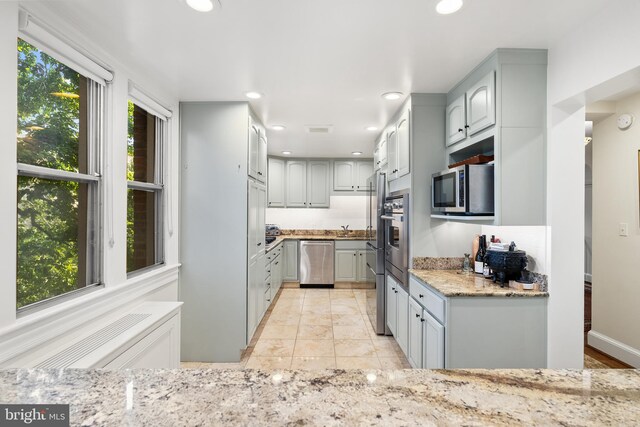 kitchen with light tile patterned floors, appliances with stainless steel finishes, light stone countertops, sink, and gray cabinets