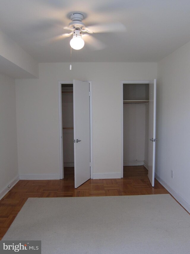 unfurnished bedroom featuring two closets, ceiling fan, and parquet flooring