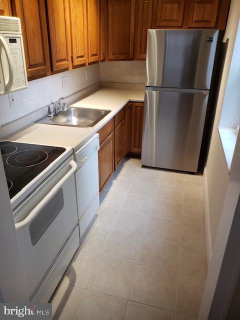 kitchen featuring brown cabinets, white appliances, light countertops, and a sink