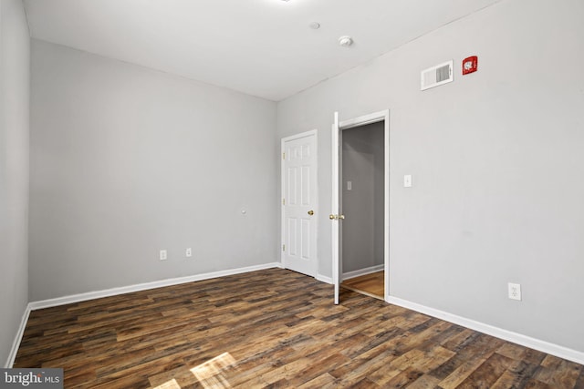 empty room featuring dark wood-style flooring, visible vents, and baseboards