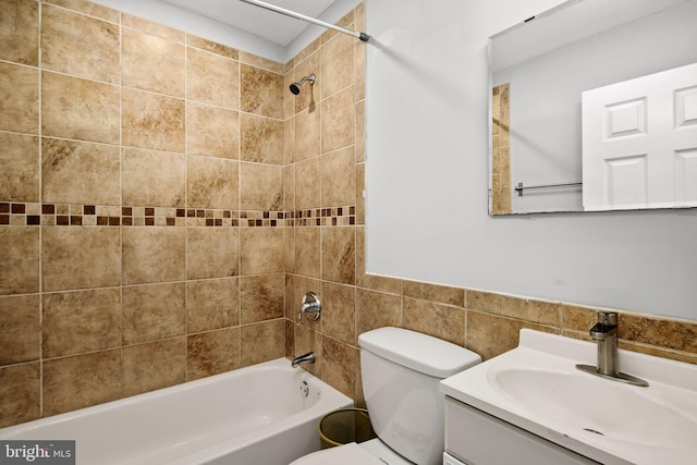 full bathroom featuring tiled shower / bath, vanity, toilet, and tile walls