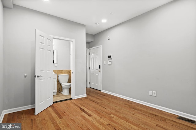 unfurnished bedroom featuring baseboards, visible vents, wood finished floors, and ensuite bathroom