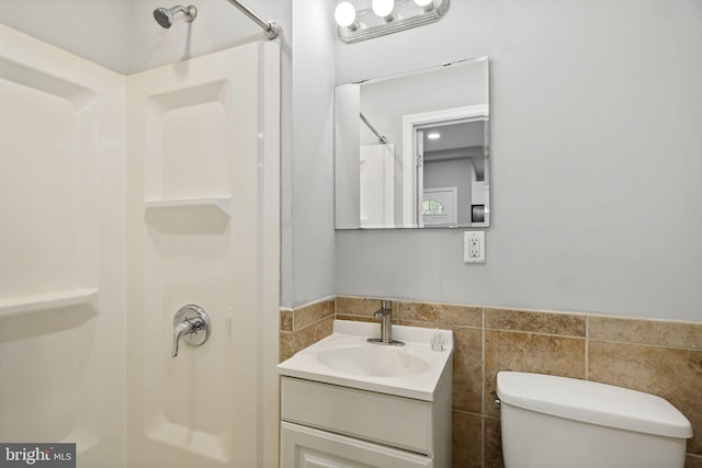 bathroom featuring tile walls, walk in shower, toilet, and vanity