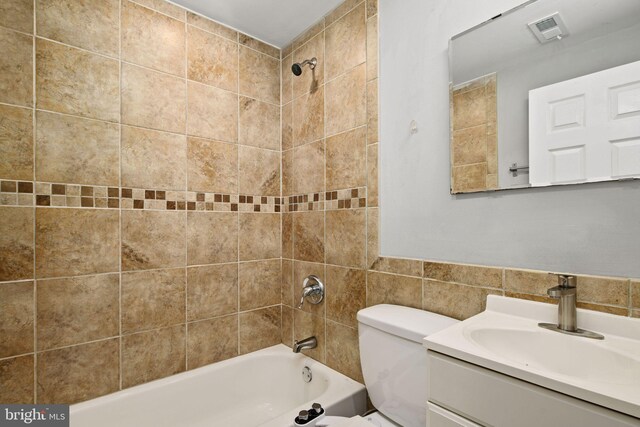 full bathroom featuring tile walls, toilet, tiled shower / bath combo, and vanity