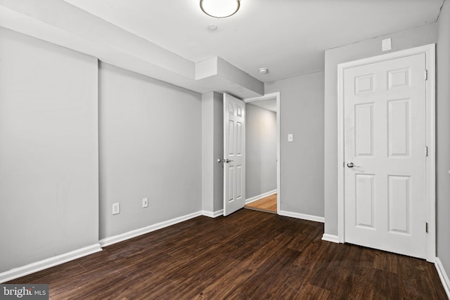 unfurnished bedroom with a closet, dark wood-style flooring, and baseboards