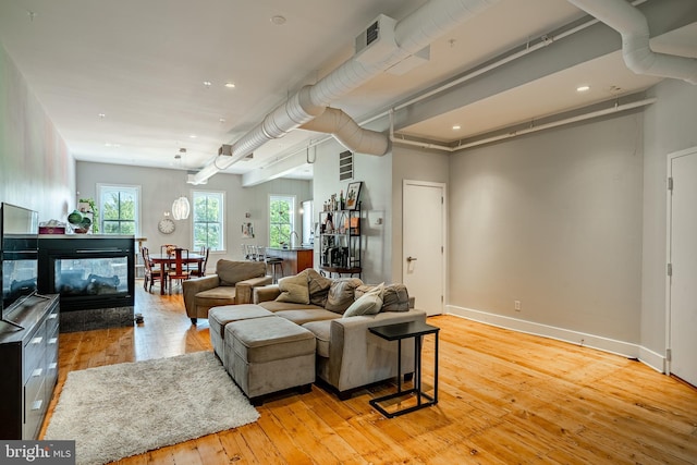 living room with recessed lighting, baseboards, a multi sided fireplace, and light wood finished floors