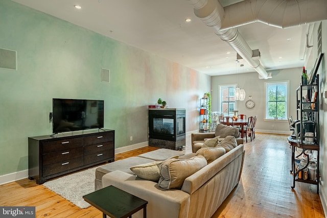 living area featuring light wood finished floors, recessed lighting, baseboards, and a multi sided fireplace