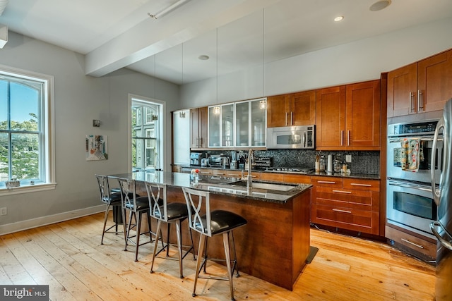 kitchen featuring light wood finished floors, decorative backsplash, brown cabinets, a kitchen breakfast bar, and stainless steel appliances