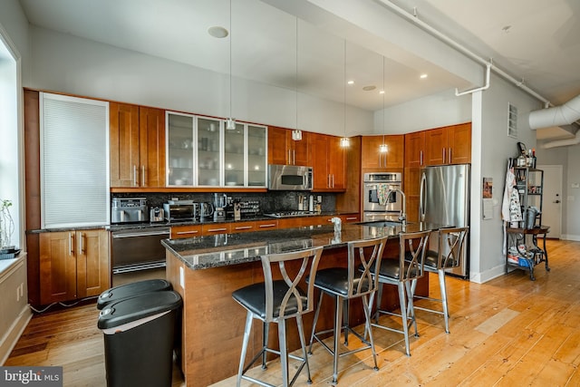 kitchen featuring a breakfast bar, light wood-style floors, appliances with stainless steel finishes, backsplash, and an island with sink