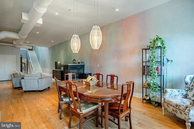 dining area featuring light wood-style floors, stairs, baseboards, and a glass covered fireplace