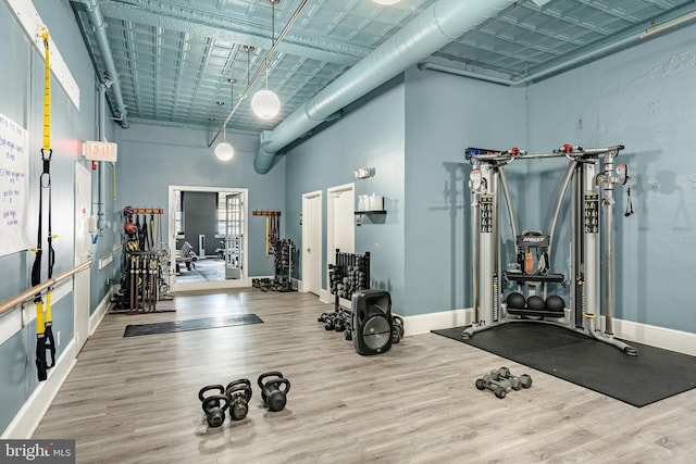 gym featuring a towering ceiling, baseboards, and wood finished floors