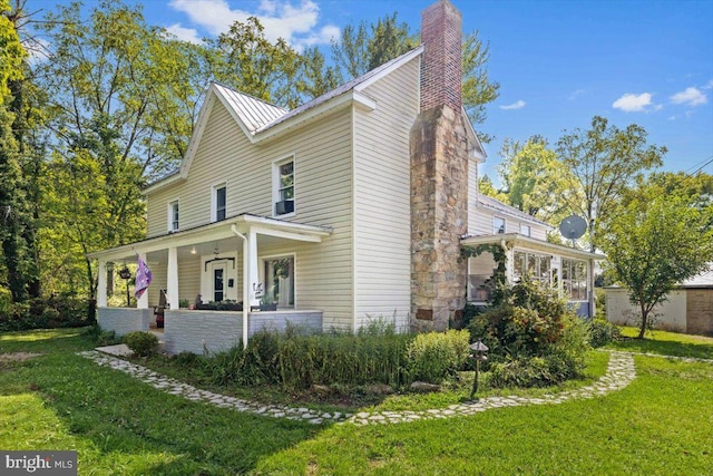 view of property exterior featuring metal roof, a porch, a yard, a standing seam roof, and a chimney