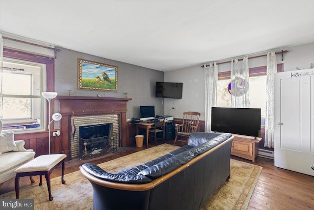 living room featuring baseboard heating, hardwood / wood-style flooring, a healthy amount of sunlight, and a brick fireplace