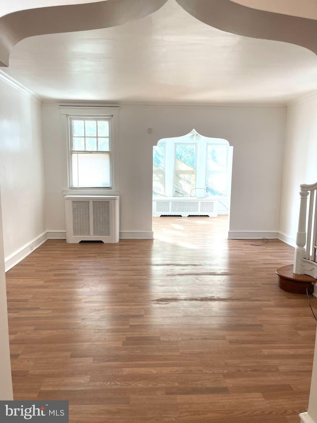 unfurnished living room featuring crown molding, wood-type flooring, and radiator