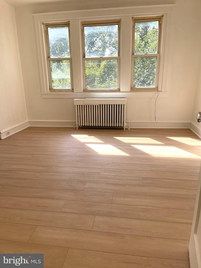 unfurnished room with light hardwood / wood-style floors, radiator heating unit, and a wealth of natural light