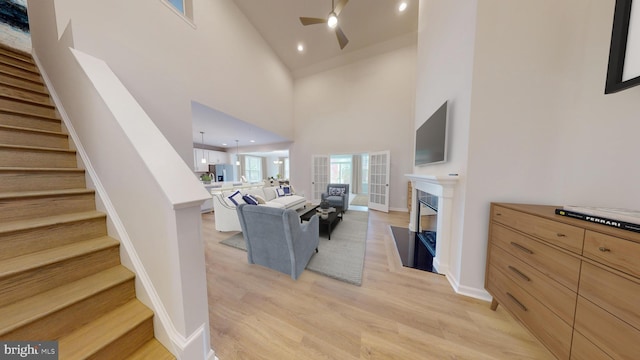 living area with light wood-type flooring, a fireplace, a towering ceiling, and stairs