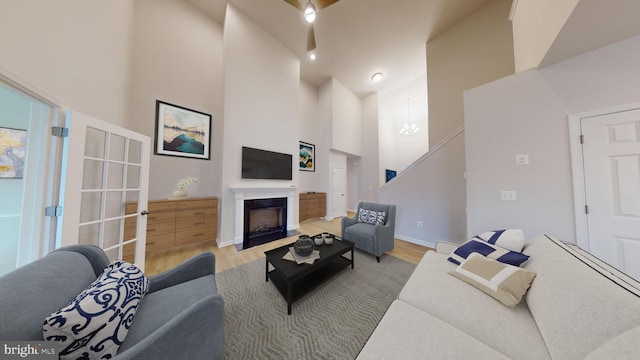 living area with a chandelier, a fireplace, a towering ceiling, and light wood-style flooring