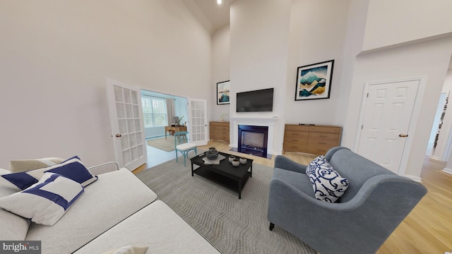 living room with a towering ceiling, a fireplace with flush hearth, wood finished floors, and french doors