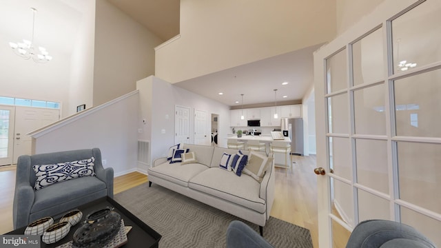 living area with an inviting chandelier, light wood-style flooring, a high ceiling, and visible vents