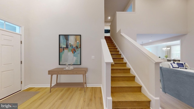 entryway featuring light wood finished floors, baseboards, stairway, a high ceiling, and a chandelier