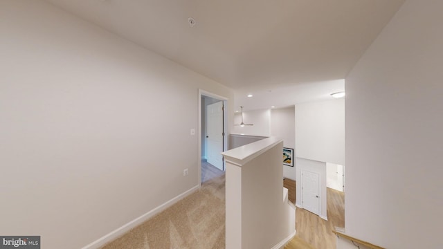 hall with light carpet, baseboards, and an upstairs landing