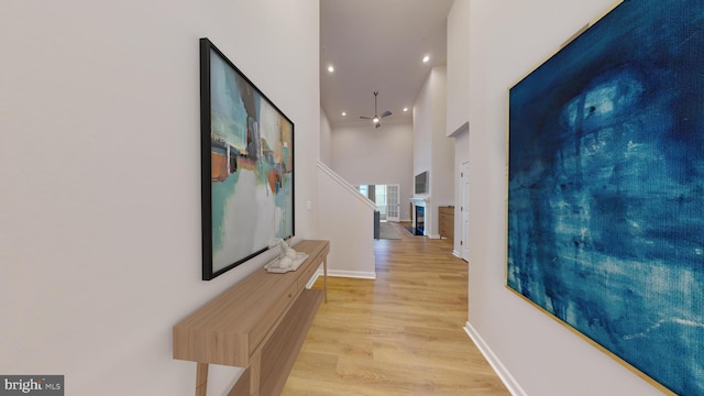 hall featuring recessed lighting, baseboards, light wood-style flooring, and a towering ceiling