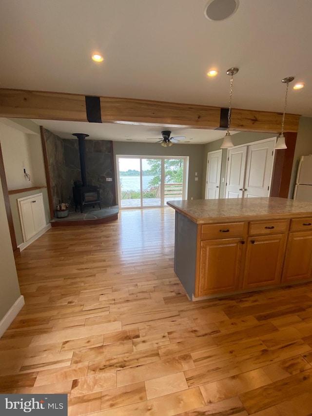 kitchen with light wood-type flooring, a wood stove, ceiling fan, white fridge, and pendant lighting